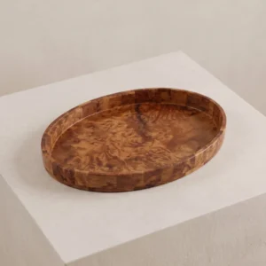 Studio angle of the handcrafted oval burl wood marquetry tray resting on a minimalist light stone pedestal.