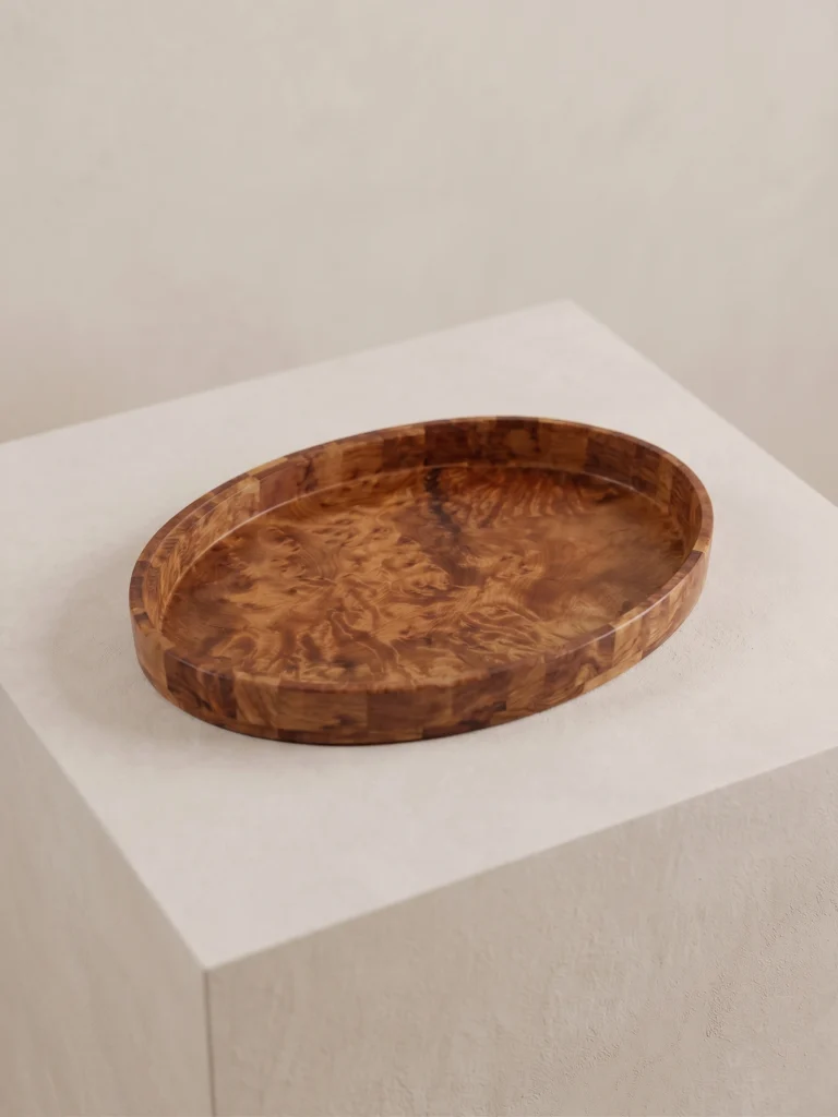 Studio angle of the handcrafted oval burl wood marquetry tray resting on a minimalist light stone pedestal.