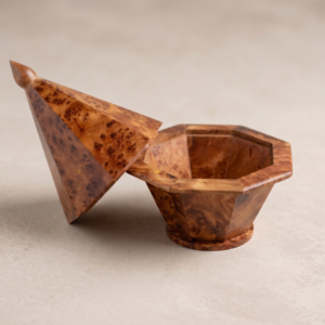 Open faceted thuya burl wood keepsake box resting on a neutral stone surface, showcasing the octagonal interior and tall geometric lid.