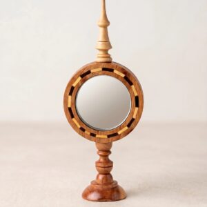 Straight-on studio view of the round thuya wood tabletop mirror, showcasing the turned pedestal base, geometric inlaid frame, and tall decorative finial on a neutral background.